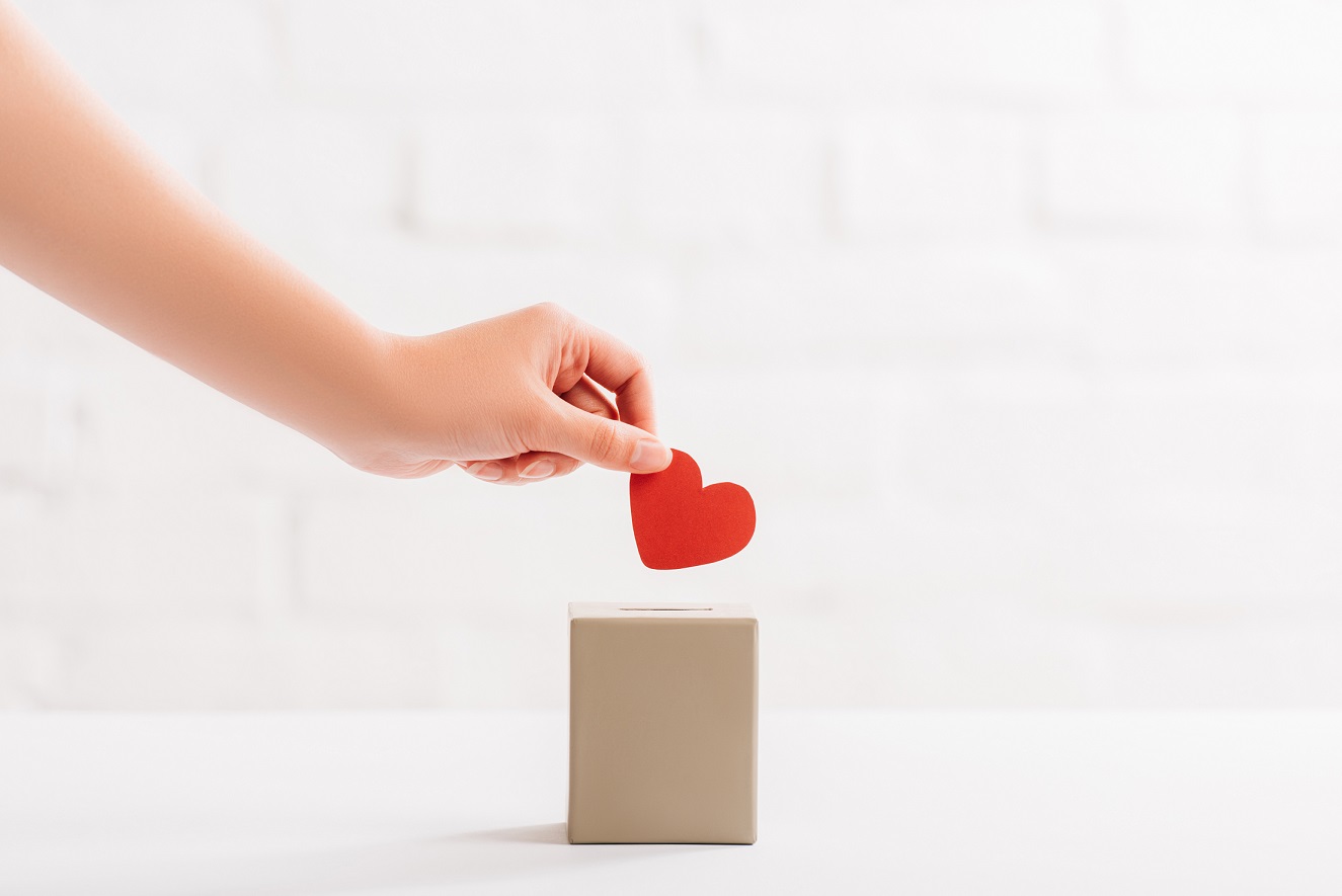 cropped view of female hand putting red heart in box on white background, donation concept cropped view of female hand putting red heart in box on white background, donation concept